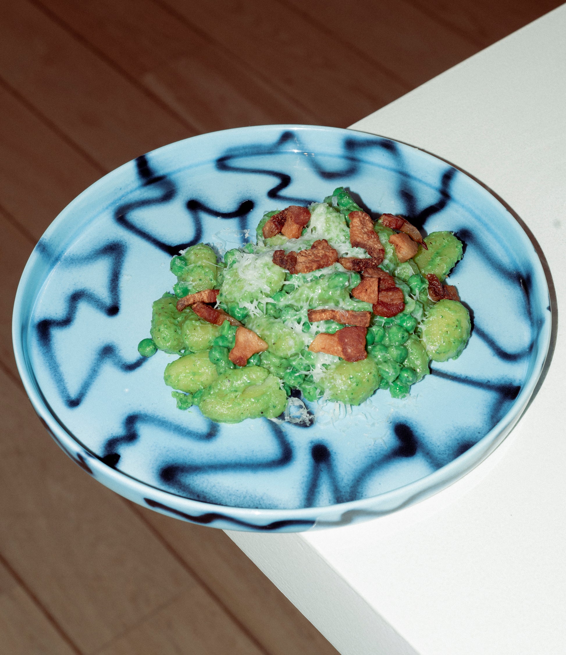 Frizbee Ceramics' Tray coming in the Blue Pizza color, holding a serving of a gnocci with peas and guanciale.