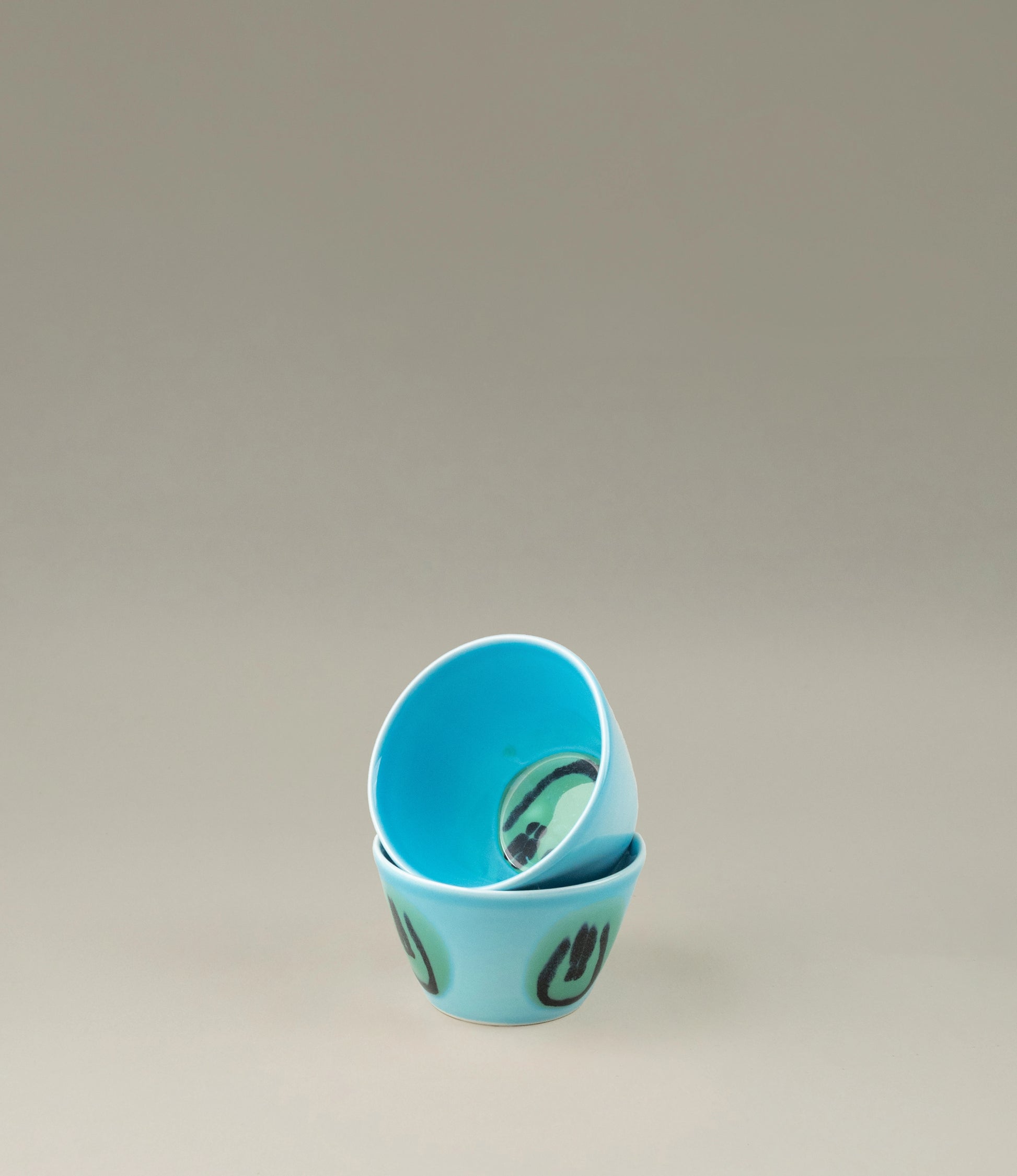 Super Cup Kawaii is an espresso sized cup from Frizbee Ceramics. The cup has a blue base with handpainted green smileys on top.