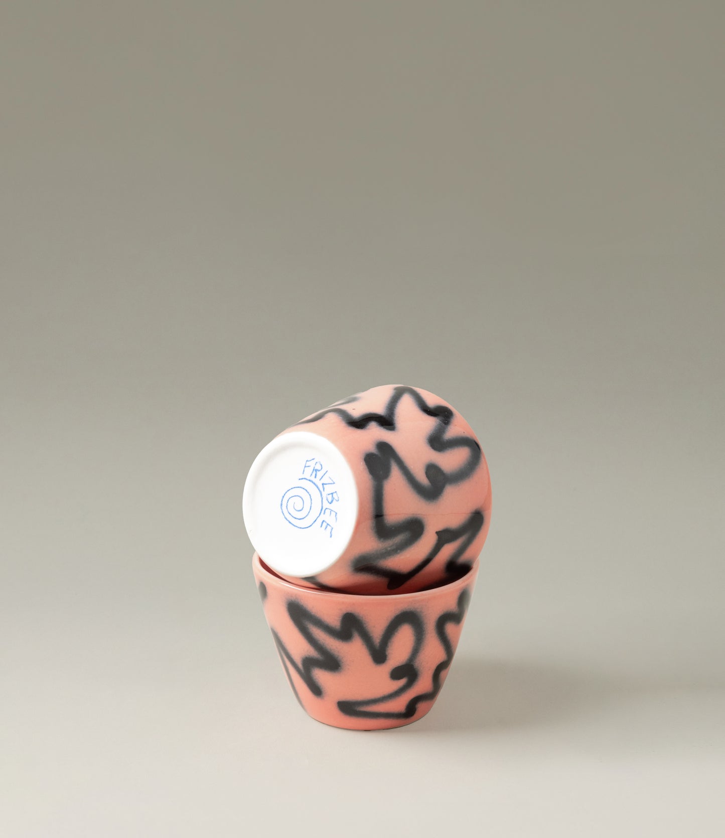 Super Cu Peach Pizza from Frizbee Ceramics is a cappucino sized cup. The product in question has a peach base with graffiti-like zig-zag pattern on top. The item is handpainted and it comes in a set of two.