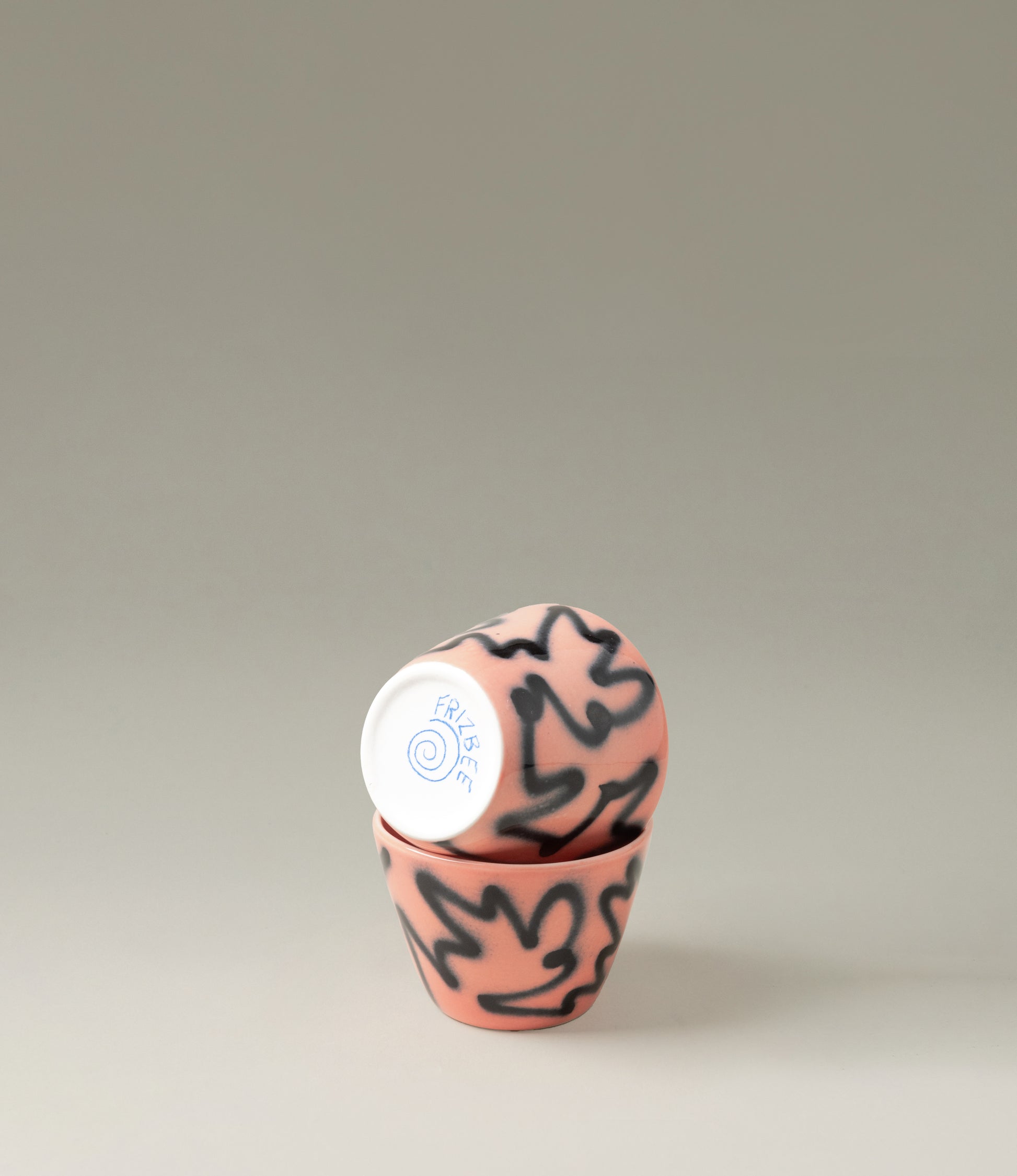 Super Cu Peach Pizza from Frizbee Ceramics is a cappucino sized cup. The product in question has a peach base with graffiti-like zig-zag pattern on top. The item is handpainted and it comes in a set of two.