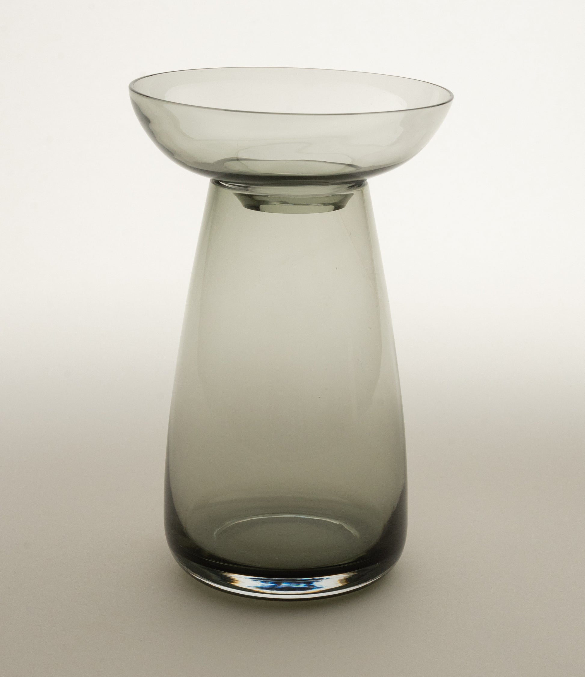 Aqua Culture Vase from Kinto is a vase to grow new plants. The vase consists of two pieces, a base and a dish for the top, which holds the bulbs, seeds or leaves. This variant has a dark, smokey gray color. 