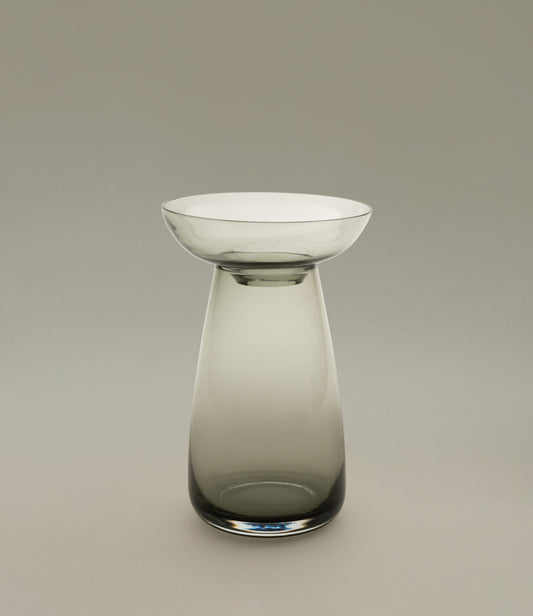 Aqua Culture Vase from Kinto is a vase to grow new plants. The vase consists of two pieces, a base and a dish for the top, which holds the bulbs, seeds or leaves. This variant has a dark, smokey gray color.