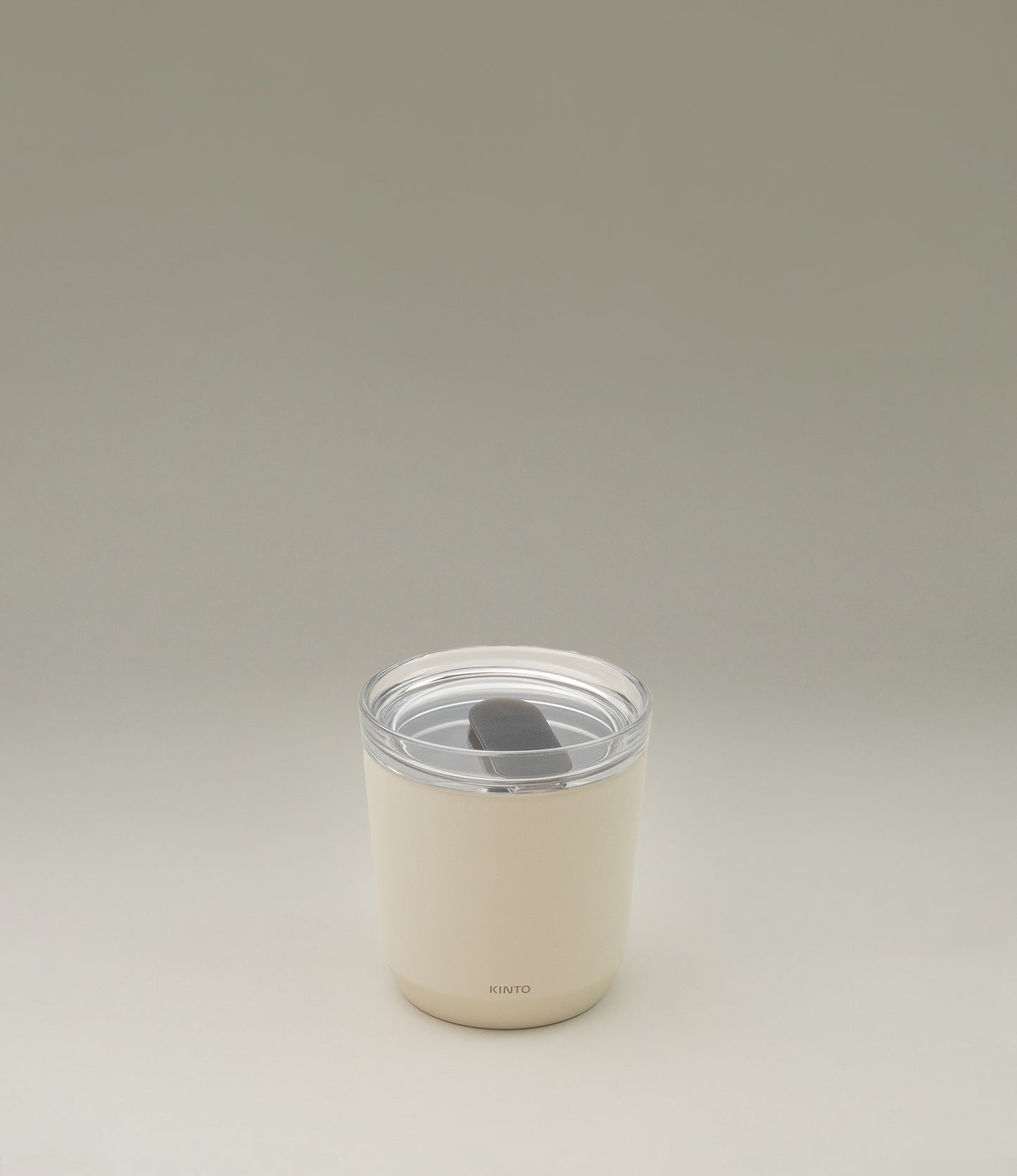 A takeaway cup from the japanese brand 'Kinto'. The To Go Tumbler is leak proof and retains the temperature and taste of your drink. The bottom of the tumbler has a matte ivory color. The top part is a clear plastic.