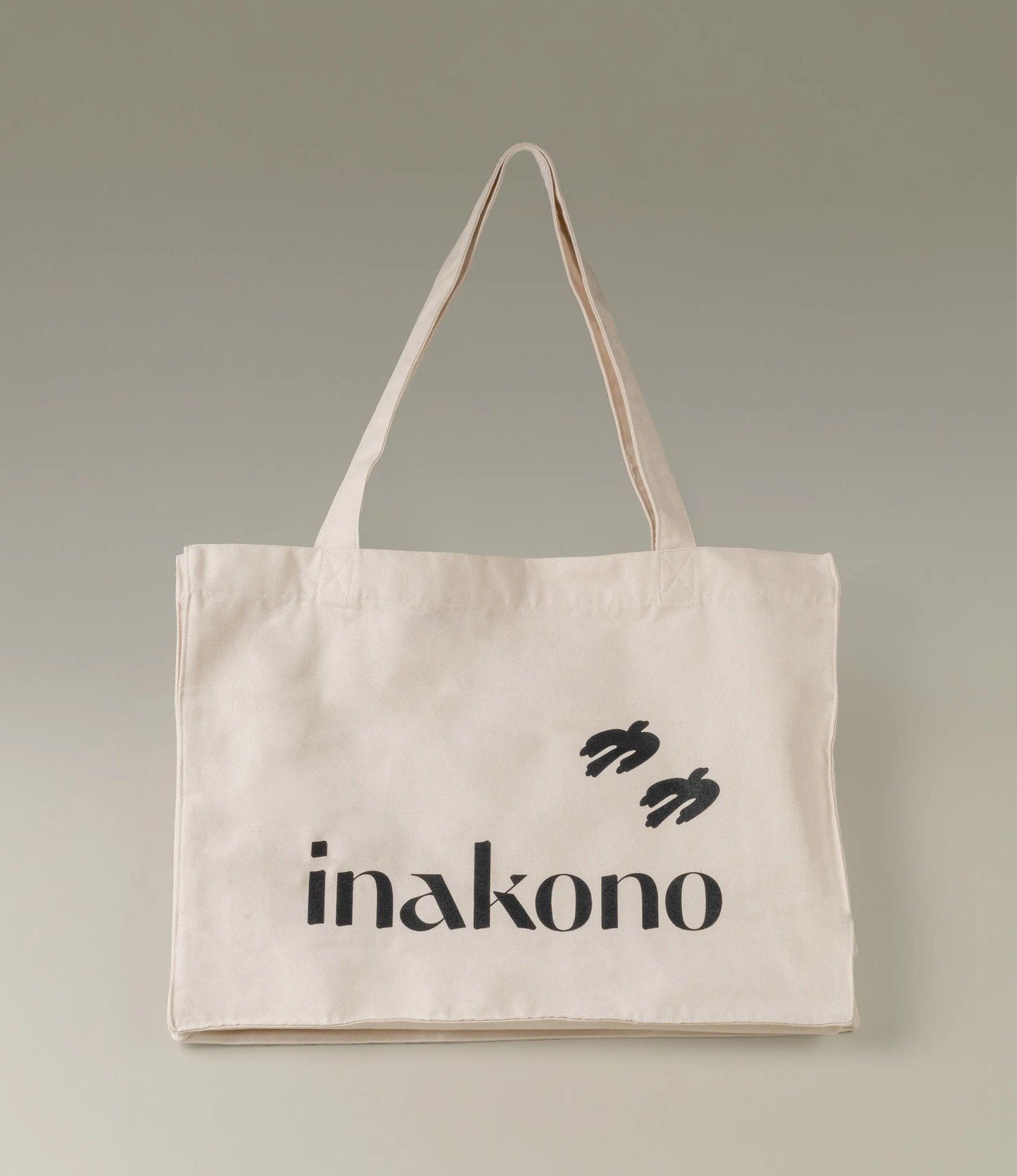 Inakono Totebag in a light base color with the soft typograhic logo of Inakono and the iconic birds printed in black.